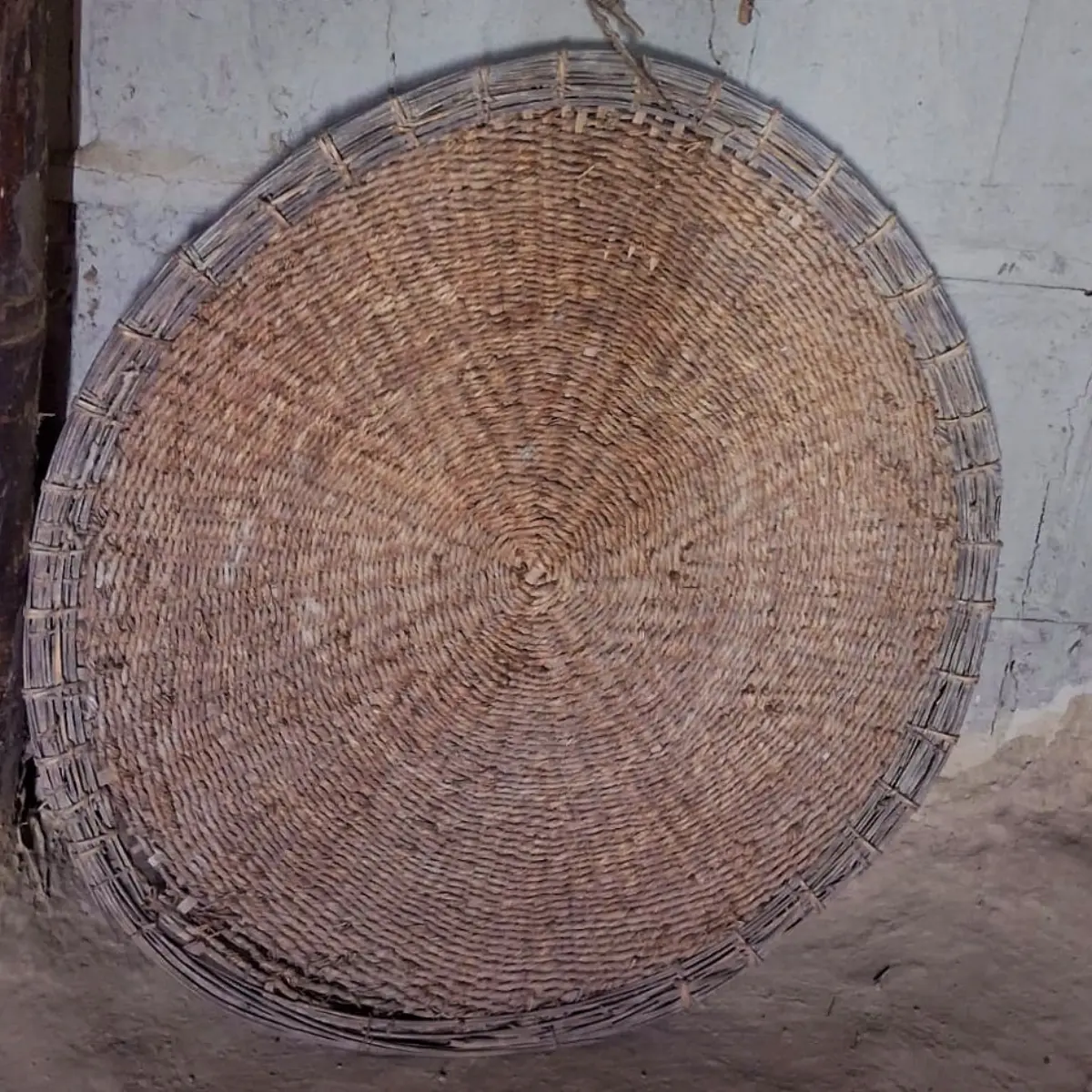 Une natte ronde tressée en herbe kuśa posée contre un mur, le siège de méditation traditionnel que nomme la Bhagavad Gita